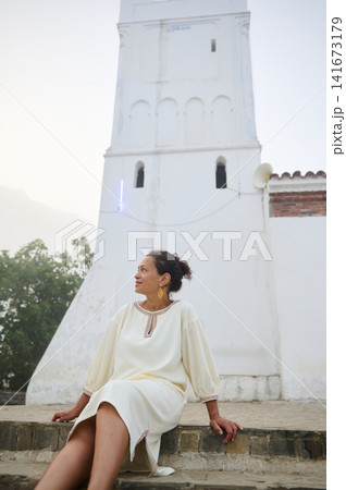 Woman in white dress sitting by a white church tower, relaxed portrait at dusk Woman in white dress sitting by a white church tower, relaxed portrait at dusk 141673179
