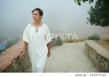 Woman walking along a foggy stone path in a white dress, calm and reflective Woman walking along a foggy stone path in a white dress, calm and reflective 141673185