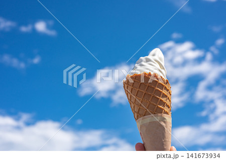 青空にソフトクリームを掲げる様子、夏のイメージ 青空にソフトクリームを掲げる様子、夏のイメージ 141673934