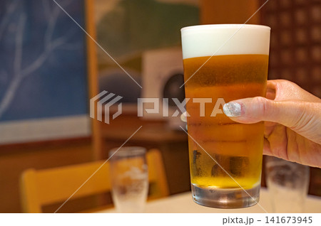 生ビールを掲げる女性の手元、乾杯のイメージ 生ビールを掲げる女性の手元、乾杯のイメージ 141673945