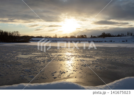 Sunset over frozen lake with scattered ice and clouds in the evening sky Sunset over frozen lake with scattered ice and clouds in the evening sky 141675023