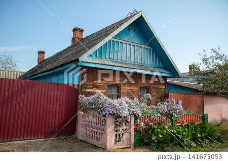 A narrow street in a village with small wooden houses and flower beds against a blue sky. A narrow street in a village with small wooden houses and flower beds against a blue sky. 141675053