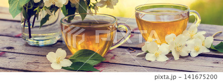 Two cups of green tea with jasmine flowers on grunge wooden table in the garden Two cups of green tea with jasmine flowers on grunge wooden table in the garden 141675200