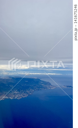 Aerial view of island coastline surrounded by deep blue ocean and layered clouds seen from airplane. Natural seascape with land, water and sky, travel and tourism concept, calm atmosphere, freedom and Aerial view of island coastline surrounded by deep blue ocean and layered clouds seen from airplane. Natural seascape with land, water and sky, travel and tourism concept, calm atmosphere, freedom and 141675246