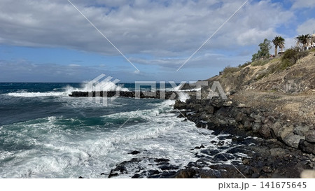 Powerful Atlantic Ocean waves crash against the volcanic rocky shoreline on Tenerife, Canary Islands, Spain. Dramatic coastal landscape with surf, rugged cliffs, copy space and travel destination. Powerful Atlantic Ocean waves crash against the volcanic rocky shoreline on Tenerife, Canary Islands, Spain. Dramatic coastal landscape with surf, rugged cliffs, copy space and travel destination. 141675645