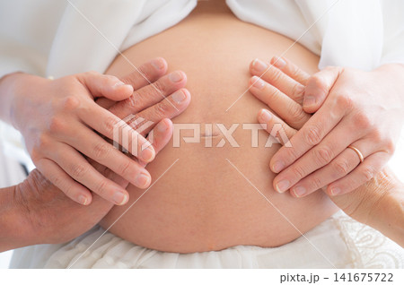 妊婦のお腹を両手で優しく包む様子、マタニティフォトのイメージ 妊婦のお腹を両手で優しく包む様子、マタニティフォトのイメージ 141675722