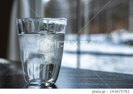 窓辺に置かれた氷入りの水のグラス、冬の情景イメージ 141675761