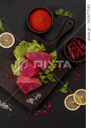 Fresh tuna steaks with lettuce, lemon, and spices on cutting board 141677545