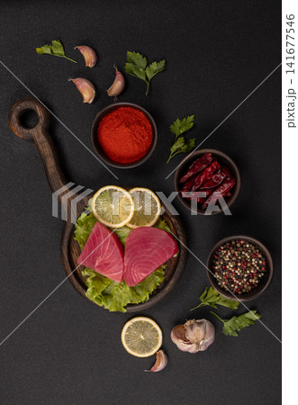 Raw tuna steaks with lemon and spices on dark background Raw tuna steaks with lemon and spices on dark background 141677546