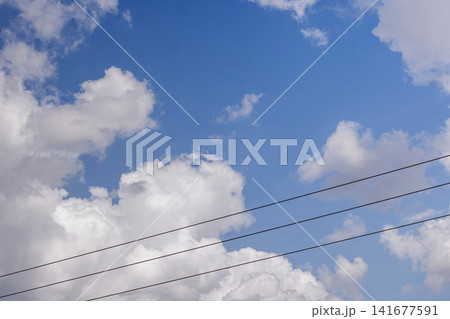 Black electrical cables and power lines stretched across a bright blue sky with clouds. High Quality Photo Black electrical cables and power lines stretched across a bright blue sky with clouds. High Quality Photo 141677591