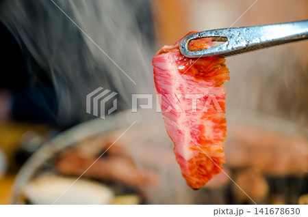 トングでつかむ霜降り肉、焼く前の新鮮な和牛 トングでつかむ霜降り肉、焼く前の新鮮な和牛 141678630