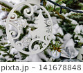 A Christmas tree stands covered in snow with ornaments attached. The scene shows details of festive decorations during wintertime 141678848