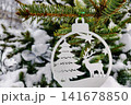 A Christmas tree is adorned with decorations in a snowy landscape. The scene shows a festive ornament featuring a tree and a deer 141678850