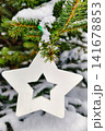 A Christmas tree stands with snow covering its branches. A white star ornament hangs from the tree. The scene captures the holiday spirit and winter atmosphere 141678853