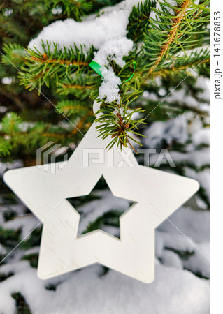 A Christmas tree stands with snow covering its branches. A white star ornament hangs from the tree. The scene captures the holiday spirit and winter atmosphere A Christmas tree stands with snow covering its branches. A white star ornament hangs from the tree. The scene captures the holiday spirit and winter atmosphere 141678853