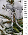 A snow-covered tree has a silver bow and a clear icicle hanging from its branches. This scene captures the holiday spirit during winter festivities 141678855