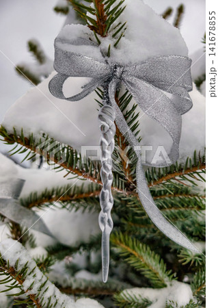 A snow-covered tree has a silver bow and a clear icicle hanging from its branches. This scene captures the holiday spirit during winter festivities A snow-covered tree has a silver bow and a clear icicle hanging from its branches. This scene captures the holiday spirit during winter festivities 141678855