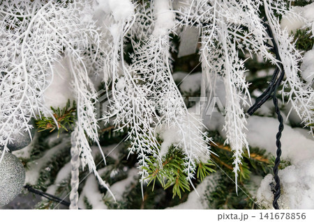 A decorated Christmas tree stands covered in snow. The tree has white accents and ornaments, creating a holiday atmosphere A decorated Christmas tree stands covered in snow. The tree has white accents and ornaments, creating a holiday atmosphere 141678856