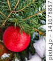 A Christmas tree stands decorated with bright red ornaments and surrounded by snow. The scene reflects holiday spirit and winter joy 141678857