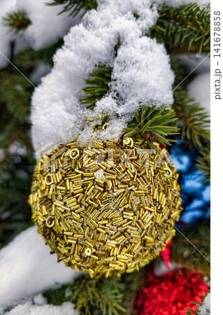 A Christmas tree ornament is covered in gold while snow falls around it. The scene captures winter festivities in a holiday setting A Christmas tree ornament is covered in gold while snow falls around it. The scene captures winter festivities in a holiday setting 141678858