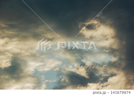 Dramatic cloudy sky with warm sunlight breaking through storm clouds Dramatic cloudy sky with warm sunlight breaking through storm clouds 141679874