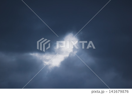 Dramatic dark storm cloud background with light glowing through a center gap Dramatic dark storm cloud background with light glowing through a center gap 141679876