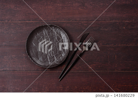 An empty round ceramic plate on a dark, textured brown background. An empty round plate An empty round ceramic plate on a dark, textured brown background. An empty round plate 141680229