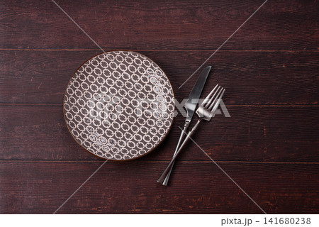 An empty round ceramic plate on a dark, textured brown background. An empty round plate An empty round ceramic plate on a dark, textured brown background. An empty round plate 141680238