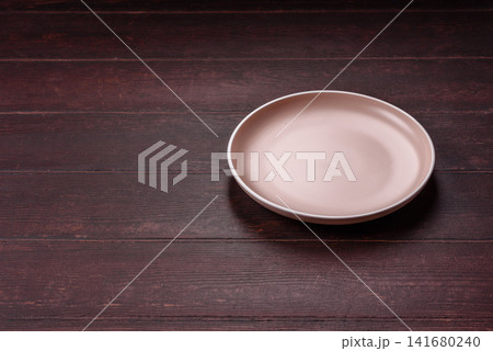 An empty round ceramic plate on a dark, textured brown background. An empty round plate An empty round ceramic plate on a dark, textured brown background. An empty round plate 141680240