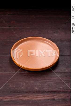 An empty round ceramic plate on a dark, textured brown background. An empty round plate An empty round ceramic plate on a dark, textured brown background. An empty round plate 141680259