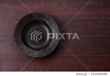An empty round ceramic plate on a dark, textured brown background. An empty round plate An empty round ceramic plate on a dark, textured brown background. An empty round plate 141680268