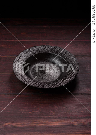 An empty round ceramic plate on a dark, textured brown background. An empty round plate An empty round ceramic plate on a dark, textured brown background. An empty round plate 141680269