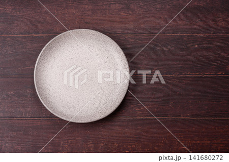 An empty round ceramic plate on a dark, textured brown background. An empty round plate An empty round ceramic plate on a dark, textured brown background. An empty round plate 141680272