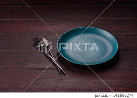 An empty round ceramic plate on a dark, textured brown background. An empty round plate An empty round ceramic plate on a dark, textured brown background. An empty round plate 141680274