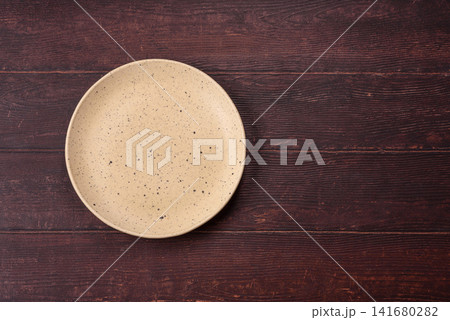 An empty round ceramic plate on a dark, textured brown background. An empty round plate An empty round ceramic plate on a dark, textured brown background. An empty round plate 141680282