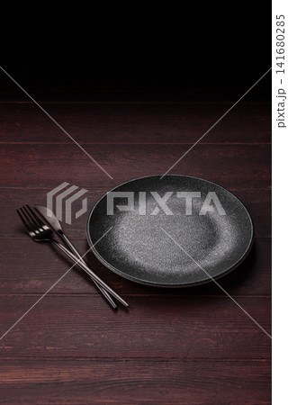 An empty round ceramic plate on a dark, textured brown background. An empty round plate An empty round ceramic plate on a dark, textured brown background. An empty round plate 141680285