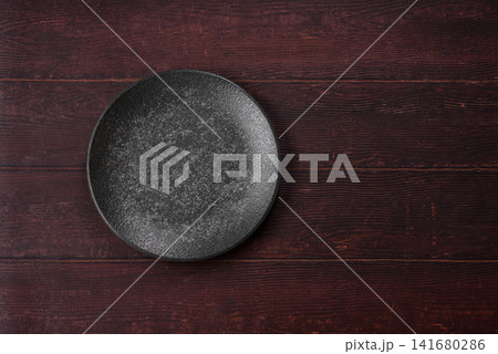 An empty round ceramic plate on a dark, textured brown background. An empty round plate An empty round ceramic plate on a dark, textured brown background. An empty round plate 141680286