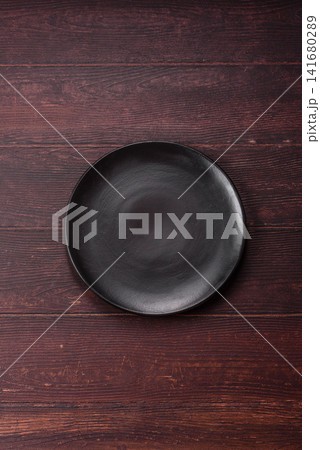 An empty round ceramic plate on a dark, textured brown background. An empty round plate An empty round ceramic plate on a dark, textured brown background. An empty round plate 141680289