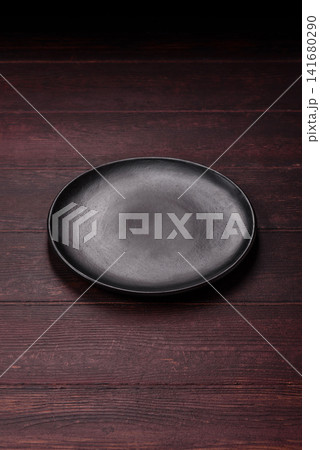 An empty round ceramic plate on a dark, textured brown background. An empty round plate An empty round ceramic plate on a dark, textured brown background. An empty round plate 141680290