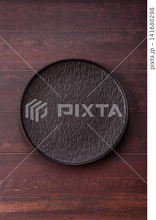 An empty round ceramic plate on a dark, textured brown background. An empty round plate An empty round ceramic plate on a dark, textured brown background. An empty round plate 141680298