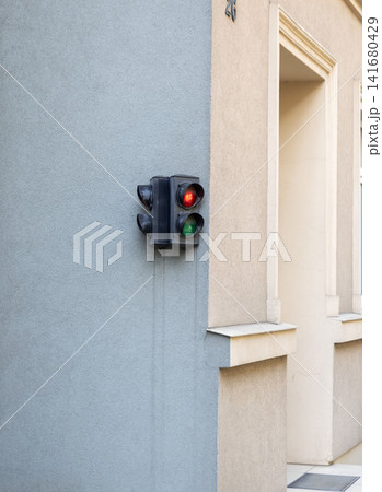 Small traffic signal mounted on beige stucco wall beside building entrance with red and green lenses, soft daylight, textured facade, recessed doorway, and calm urban architectural detail Small traffic signal mounted on beige stucco wall beside building entrance with red and green lenses, soft daylight, textured facade, recessed doorway, and calm urban architectural detail 141680429