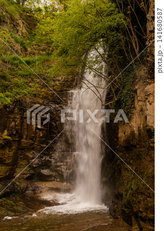 Majestic Waterfall Cascading Down a Steep Rocky Cliff Surrounded by Lush Green Vegetation and Fores Majestic Waterfall Cascading Down a Steep Rocky Cliff Surrounded by Lush Green Vegetation and Fores 141680587