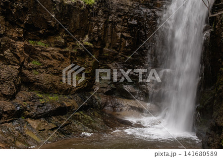 Majestic Waterfall Cascading Down a Steep Rocky Cliff Surrounded by Lush Green Vegetation and Fores Majestic Waterfall Cascading Down a Steep Rocky Cliff Surrounded by Lush Green Vegetation and Fores 141680589