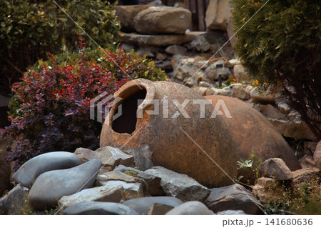 Ancient Clay Amphora Resting Near Weathered Log in Rustic Garden Landscape Historic Pottery Artifac 141680636