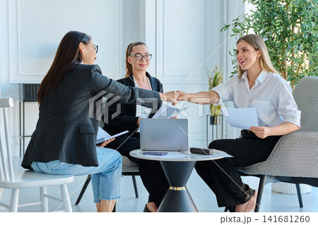 Businesswomen giving fist bump during successful teamwork meeting in modern office Businesswomen giving fist bump during successful teamwork meeting in modern office 141681260