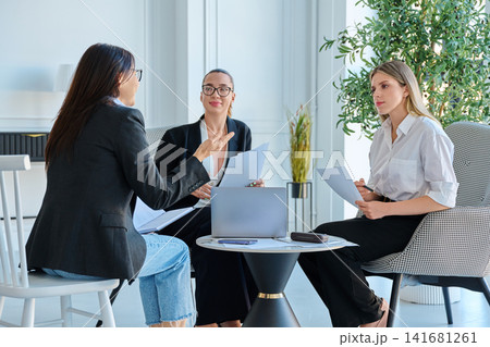 Group of diverse businesswomen discussing project documents during meeting in office Group of diverse businesswomen discussing project documents during meeting in office 141681261