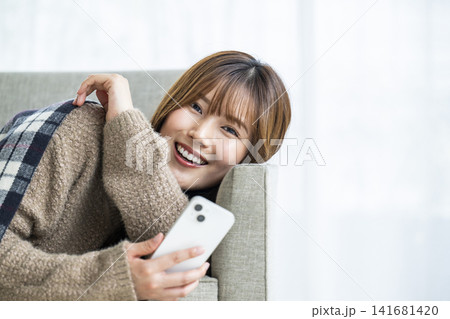 部屋でスマホを操作する若い女性 部屋でスマホを操作する若い女性 141681420