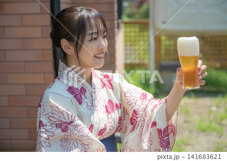 浴衣姿でビールを掲げる女性、乾杯の笑顔 浴衣姿でビールを掲げる女性、乾杯の笑顔 141683621