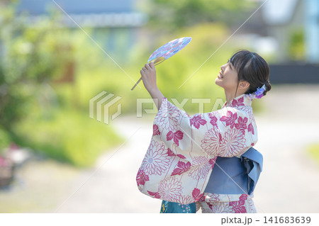 うちわを高く掲げる浴衣女性、開放的な夏の一枚 うちわを高く掲げる浴衣女性、開放的な夏の一枚 141683639