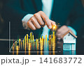 Businessman hand placing coin on stack with rising stock chart and wooden house model, real estate investment and financial growth concept. 141683772